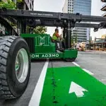Thumbnail of Omega Morgan Machinery moving crew driving green lift in downtown Seattle.